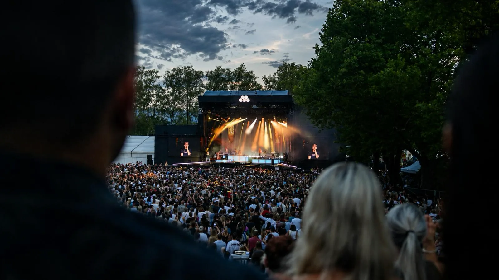 Audience in front of the stage at dusk, with the big screen alongside